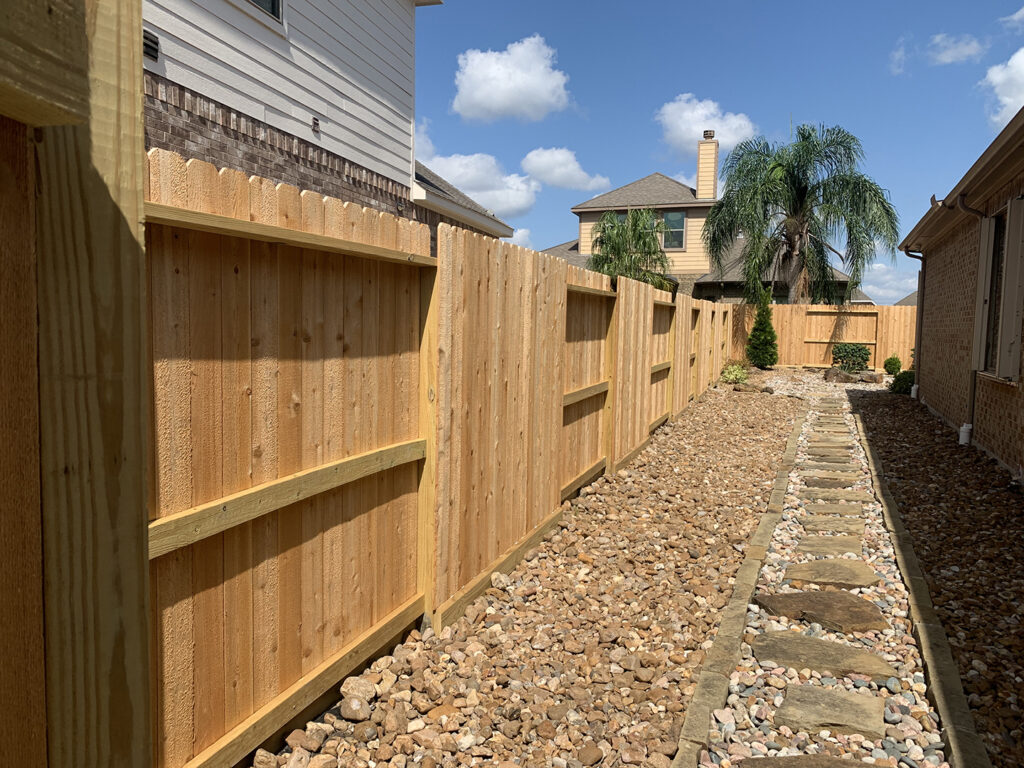 Cedar fence with palm tree and rocky landscaping